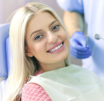 Woman patient smiling in dental chair after a teeth whitening treatment.